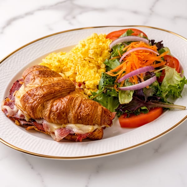 Breakfast plate with a ham and cheese croissant, scrambled eggs, and a side salad.
